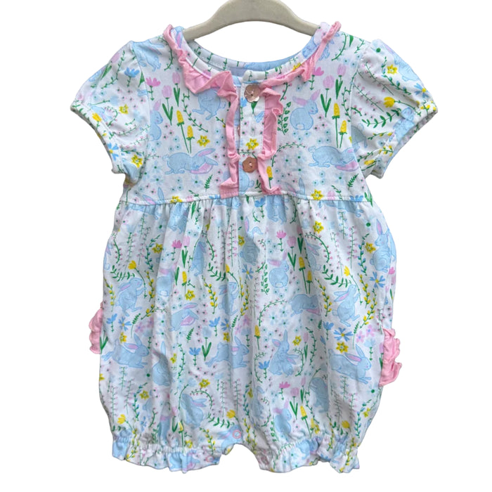 A baby romper with a light blue and white floral print, pink ruffle trim, and pink bow details, hanging on a white plastic hanger against a brick wall.