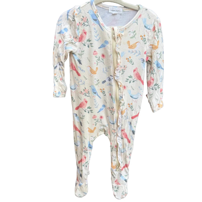 A baby footed one-piece sleeper with a colorful bird and floral print on a cream background, hanging on a wooden hanger against a brown brick wall.