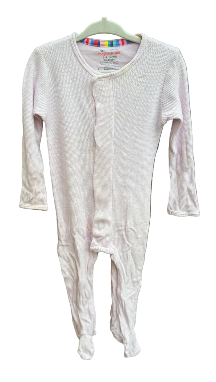 A light pink long-sleeve baby footed sleeper hanging on a hanger against a brick wall background.