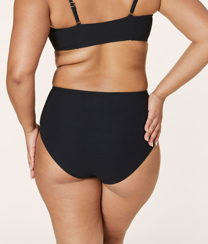 Back view of Andie Swim eco ribbed black high waisted bottom, featuring full seat coverage, low leg cut, and compressive fabric on curvy model