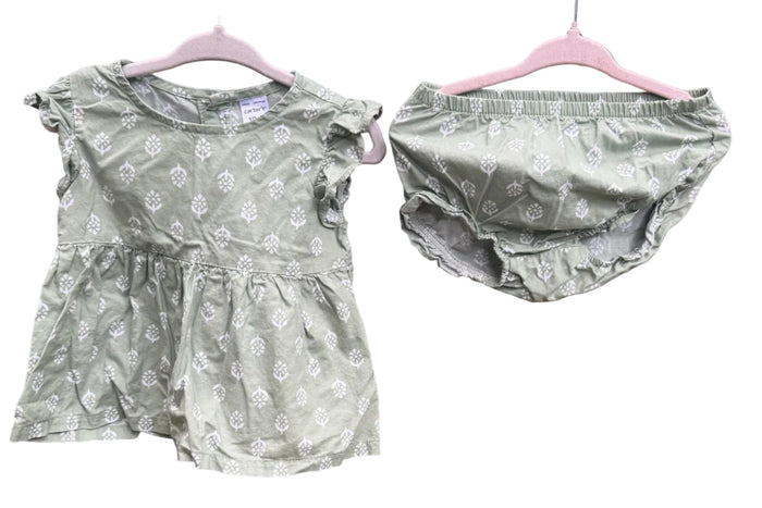 A baby girl's two-piece outfit consisting of a short-sleeve ruffle-sleeve top and matching diaper cover, both in sage green with a white floral pattern, hanging on pink hangers against a red brick wall.
