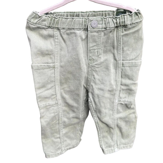 A pair of light sage green denim shorts hanging on a white plastic hanger against a red-brown brick wall.