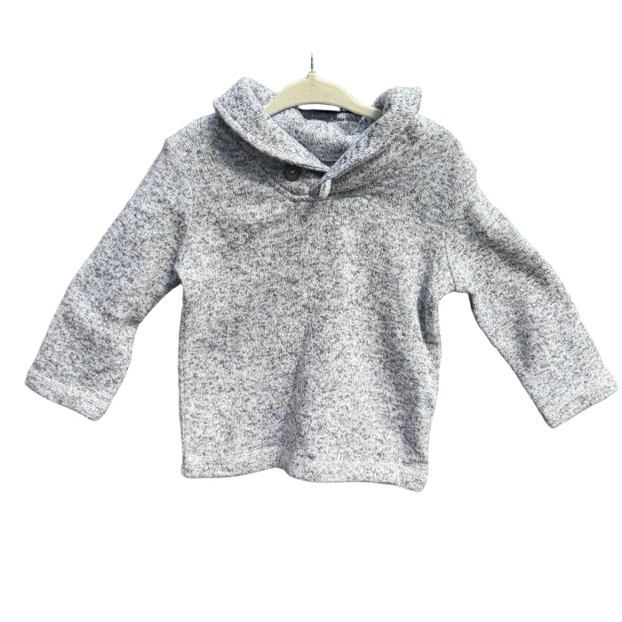 A light gray marled knit hooded sweater with three-quarter sleeves hangs on a wooden hanger against a brick wall with green trees in the background.