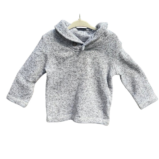 A light gray marled knit hooded sweater with three-quarter sleeves hangs on a wooden hanger against a brick wall with green trees in the background.