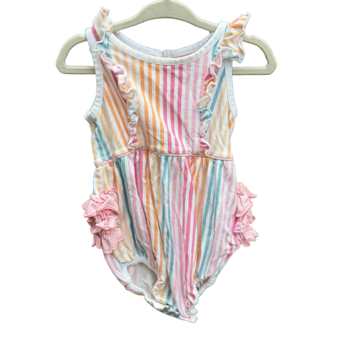A baby girl's sleeveless romper with pastel vertical stripes in pink, orange, yellow, blue, and white, featuring ruffle details on the shoulders and hips, hanging on a white plastic hanger against a brown brick wall.