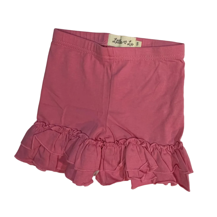 A pink ruffled mini skirt laid flat on a white sheet, with a small white brand label visible at the waistband.