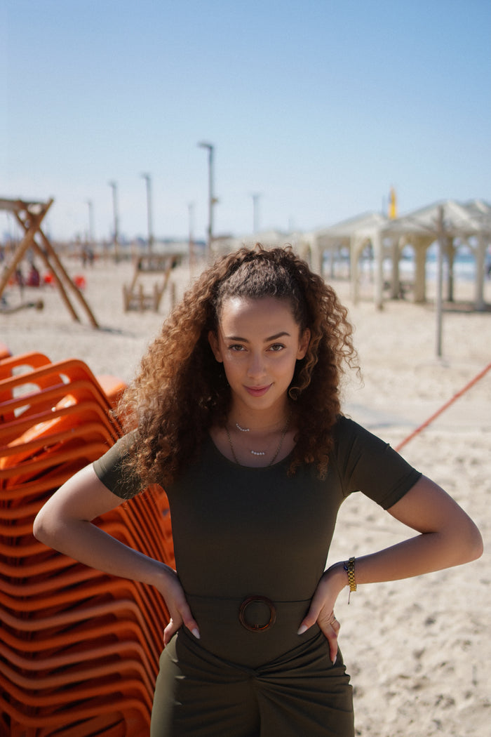 A woman standing on a beach wearing a green one-piece swimsuit