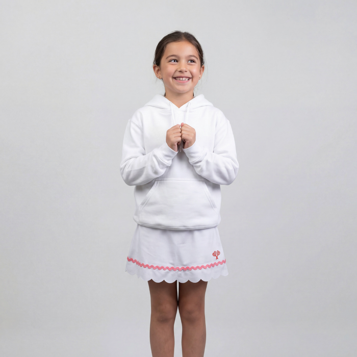 Young girl wearing a white hoodie and skirt with pink trim on a light gray background