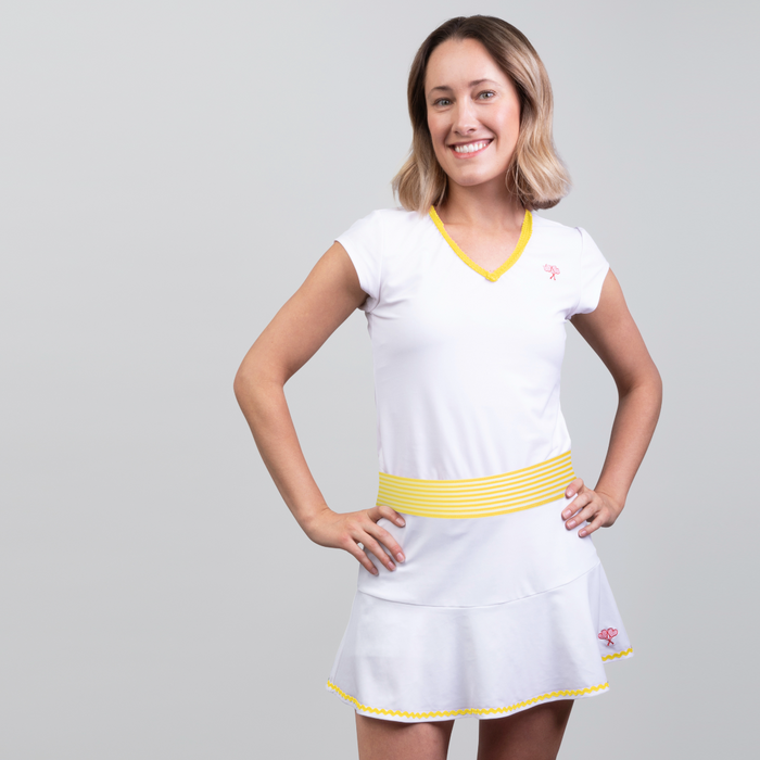 Woman wearing a white tennis dress with yellow accents on a gray background