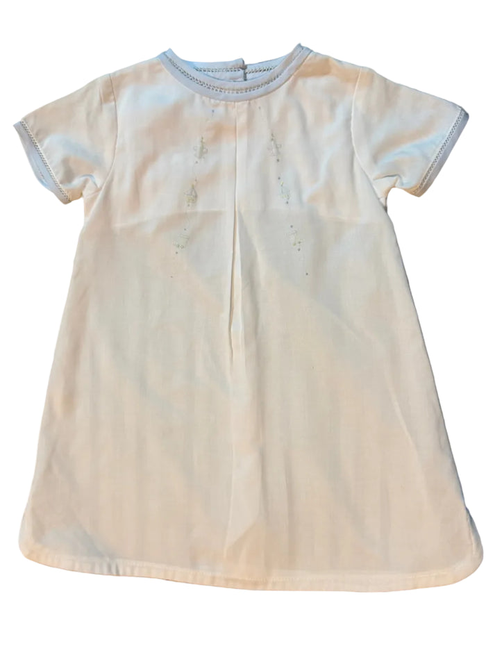 A white short-sleeve baby t-shirt with a center back opening and subtle embroidered details, laid flat on a striped gray and white surface.