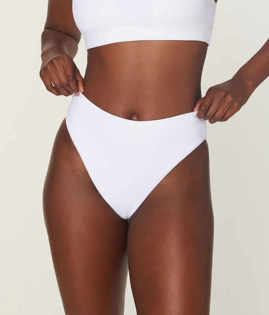 Model adjusting high-waist white Andie Swim bikini bottom, showing a close-up of the compressive fabric and high-rise design.