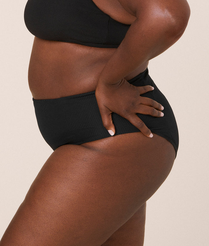 Andie Swim high-waisted cheeky black bikini bottom with a side view, showcasing the high rise and cheeky cut in ribbed, eco-friendly fabric.