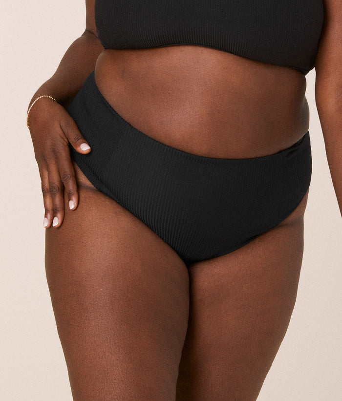 Andie Swim high-waisted cheeky black bikini bottom with flattering side seams and ribbed texture, modeled from the front. Vintage-inspired, compressive fit