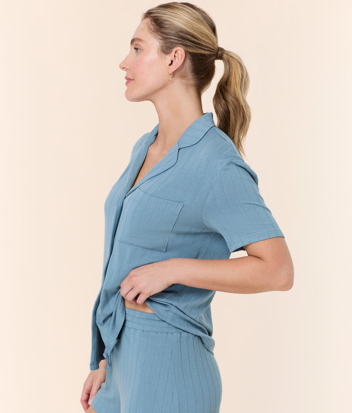 Side view of model wearing Andie Swim Infinity Blue Short Sleeve Button Up, featuring a button-down front and collar.